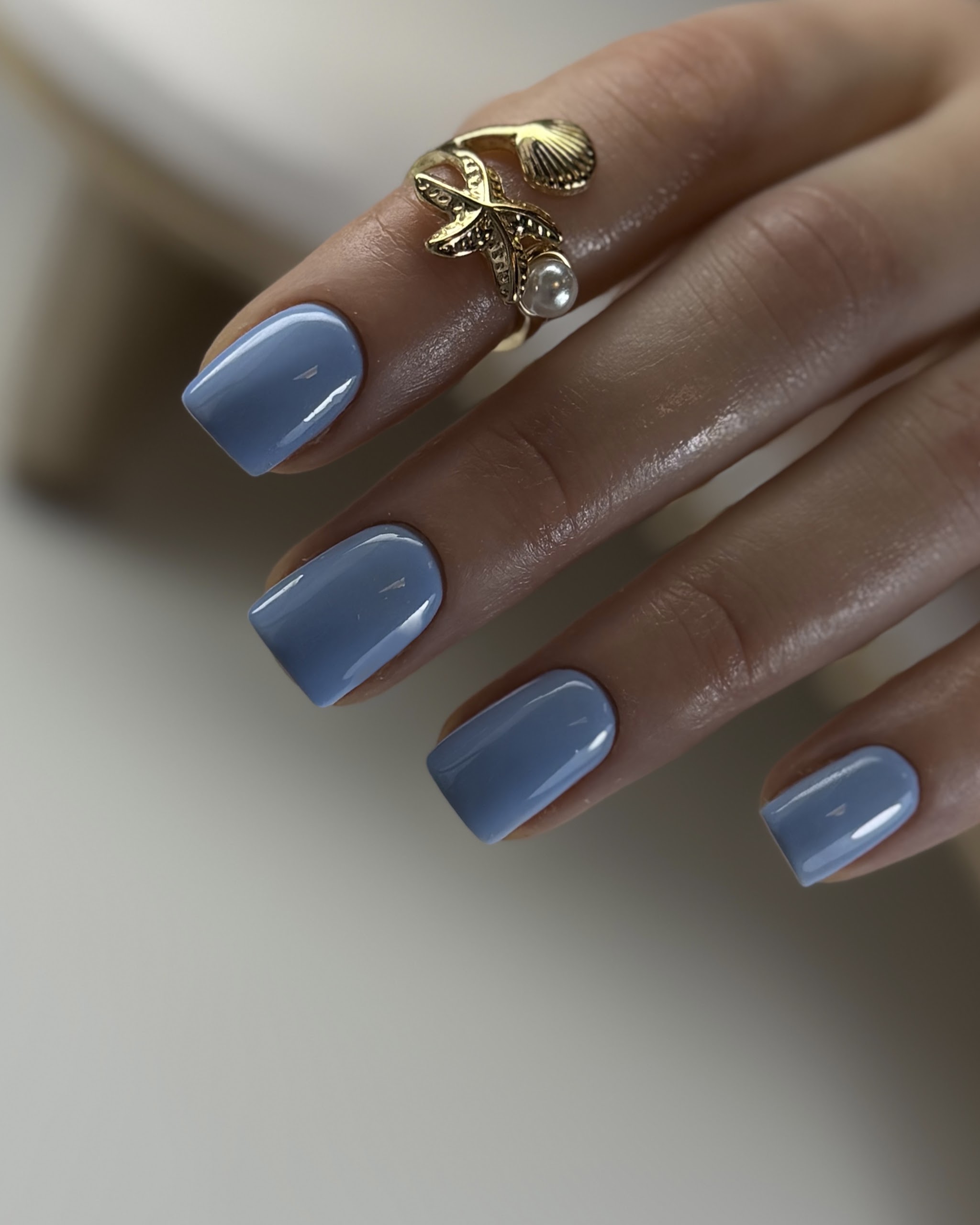 Vierkante nagels met blauwgrijze gellak en een gouden ring