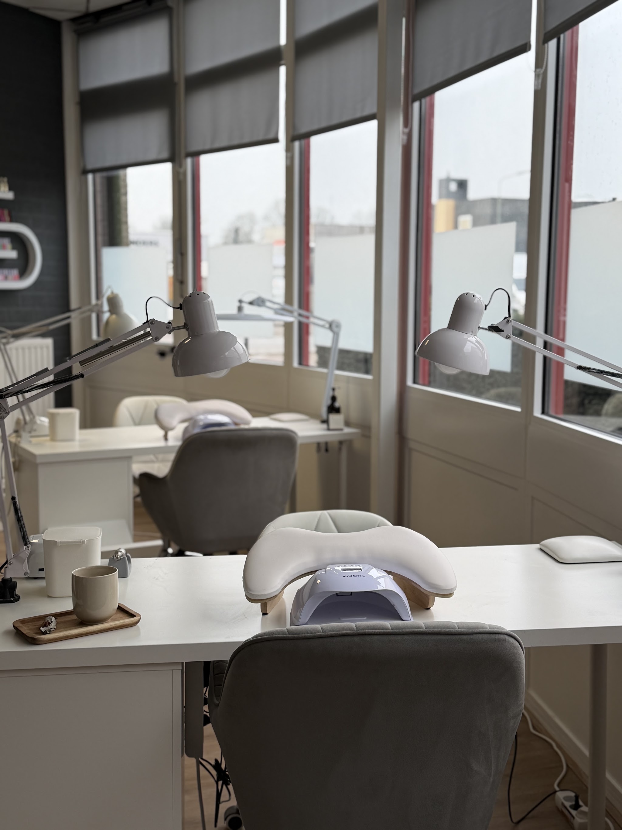 De salon met nageltafels, lampen en stoelen bij de grote ramen